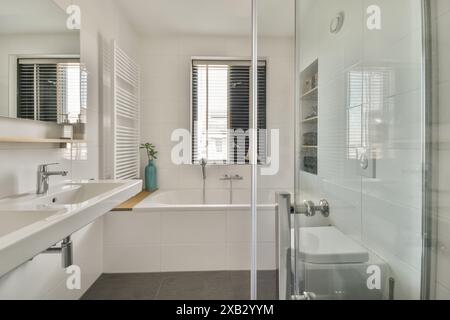 Das moderne Badezimmer in der Duintopstraat verfügt über weiß geflieste Wände, eine große Badewanne, einen Waschtisch mit zwei Waschbecken und eine Glasdusche mit natürlichem Licht Stockfoto
