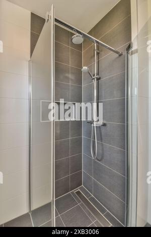 Dieses Bild verfügt über ein modernes Badezimmer mit einer modernen Duschkabine, mit grauen gefliesten Wänden, einer Glastür und Edelstahlfächern Stockfoto