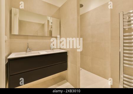 Ein modernes Badezimmer mit einem an der Wand montierten Schminktisch mit großem Spiegel, gefliesten Wänden in neutralem Beige und minimalistischem Design. Stockfoto