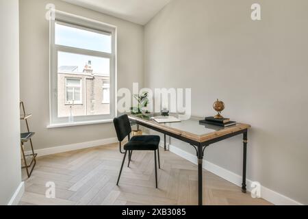 Ein helles Home Office mit großem Fenster, Fischgrätenboden und stilvollem Holzschreibtisch mit grünem Samtstuhl. Stockfoto