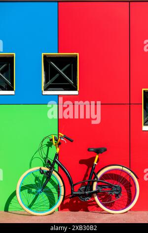 Ein in kräftigen Farben gehaltenes Fahrrad lehnt sich an eine farbenfrohe Wand mit geometrischen Mustern, die eine verspielte urbane Ästhetik in Szene setzt Stockfoto