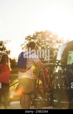 Ein junger Mann und eine Frau bereiten sich auf das Geländeradfahren vor und nehmen Elektro-Mountainbikes vom Fahrradträger im Wohnmobil ab. Stockfoto