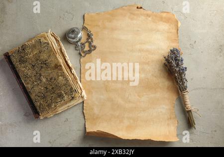 Blatt altes Pergamentpapier, Lavendelblumen, Vintage-Buch und Taschenuhr mit Kettenkette auf grauem Tisch, flach gelegen Stockfoto