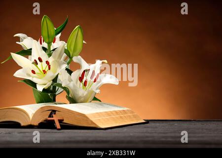 Bibel, Kreuz und Lilien auf grauem Tisch vor braunem Hintergrund, Platz für Text. Religion des Christentums Stockfoto