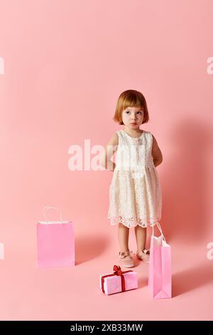 Entzückendes Mädchen in weißem Kleid mit Geschenktüten vor rosa Hintergrund. Stockfoto