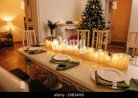 Ein gemütliches, stilvolles Wohnzimmer mit einem überdachten Tisch und einem dekorierten Weihnachtsbaum mit einer Girlande. Ein festliches Mittagessen oder eine Party. Beleuchtete Kerzen, Teller und Stockfoto