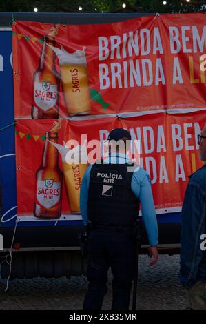 Ein Polizist steht vor einem hellen Banner, das Sagres Beer bei den alfama-Festlichkeiten anpreist und überwacht die lebhafte Veranstaltung Stockfoto