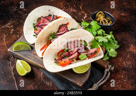 Carne Asada Tacos mit gegrilltem Steak, grüner Sauce, Jalapenos und Zwiebeln, mexikanische Küche. Dunkler Hintergrund. Draufsicht. Stockfoto