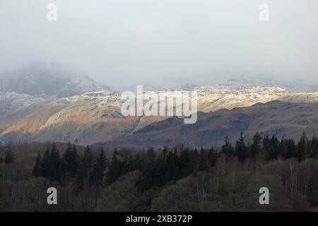 Sonnenlicht, das die schneebedeckten Fjäle von Loughrigg und Blea Rigg aus der Nähe von Waterhead Ambleside im Lake District England einfängt Stockfoto