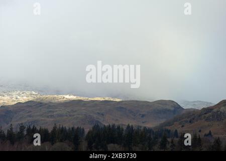 Sonnenlicht, das die schneebedeckten Fjäle von Loughrigg und Blea Rigg aus der Nähe von Waterhead Ambleside im Lake District England einfängt Stockfoto