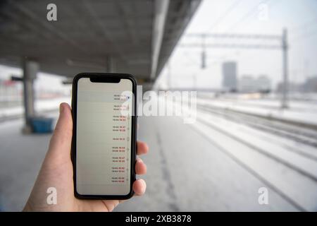 Hand eines Mannes, der am Bahnhof ein Smartphone hält Stockfoto
