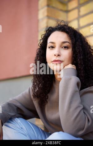 Schöne junge Frau, die an der Wand sitzt Stockfoto