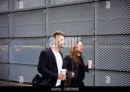 Reifer Geschäftsmann und Geschäftsfrau mit Einwegbechern, die an der Gitterwand vorbeigehen Stockfoto
