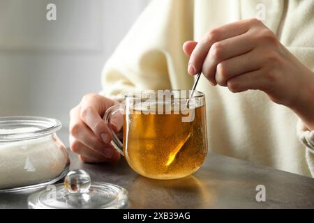 Frau rührt Zucker in Tee an einem grauen Tisch, Nahaufnahme Stockfoto