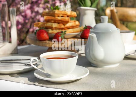 Frisch gebackene Waffeln und eine Tasse Tee auf dem Tisch im Garten Stockfoto