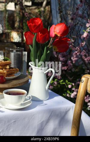 Wunderschöner Tulpenstrauß und frisch gebackene Waffeln auf dem Tisch, serviert zum Teetrinken im Garten Stockfoto