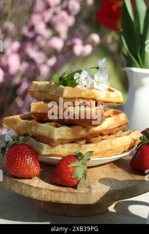 Frisch gebackene Waffeln und ein wunderschöner Tulpenstrauß auf dem Tisch im Garten, Nahaufnahme Stockfoto