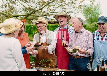 Eine Gruppe älterer Freunde, die gemeinsam im Freien Bücher singen und lesen, feiern Freundschaft und Freude in einem geselligen Treffen. Stockfoto