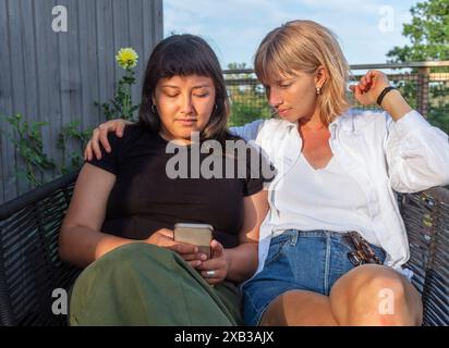 Junge Freundinnen, die auf dem Stuhl sitzen und ihr Smartphone benutzen Stockfoto