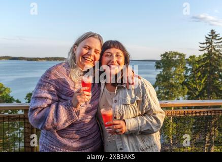 Glückliche Freundinnen mit Cocktails, die vor dem Meer stehen Stockfoto