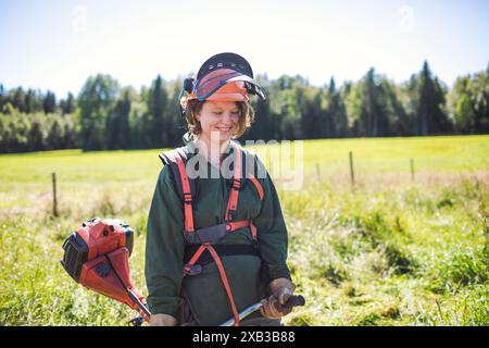 Lächelnde Frau, die Arbeitskleidung trägt und Unkrautschneider im Hof hält Stockfoto