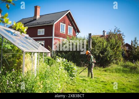 Frau, die während des sonnigen Tages im Garten Gras mäht Stockfoto