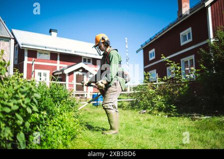 Frau, die während des sonnigen Tages Gras im Hof mäht Stockfoto