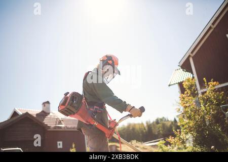 Frau mit Unkrautschneider im Garten gegen den Himmel während des sonnigen Tages Stockfoto