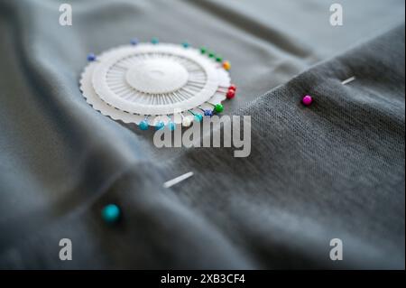 Näh-Nadeln liegen auf Stoff, der gesäumt wird. Das Bild erfasst den Nähprozess und betont die Werkzeuge und die Präzision, die für das Säumen von Stoff erforderlich sind Stockfoto