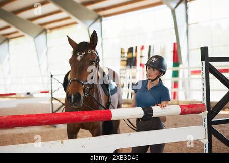 Jockey-Frau, die beim Training auf der Ranch mit Pferd am Hindernis steht Stockfoto