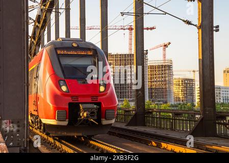 Elektrischer Pendlerzug auf einer steilen Eisenbahnbrücke über einen Fluss bei Sonnenuntergang im Sommer Stockfoto