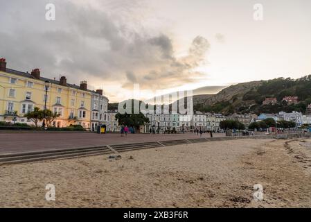 Menschen, die an der von pastellfarbenen Gebäuden gesäumten Promenade in der Küstenstadt Llandudno bei Sonnenuntergang spazieren Stockfoto