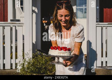 Fröhliche junge Frau, die frischen Erdbeerkuchen am sonnigen Tag im Hinterhof trägt Stockfoto