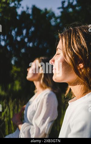 Seitenansicht einer jungen Frau mit geschlossenen Augen, die von einem Freund sitzt und Sonnenlicht genießt Stockfoto
