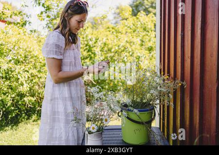 Seitenansicht einer jungen Frau, die Blumen im Eimer im Hinterhof sammelt Stockfoto