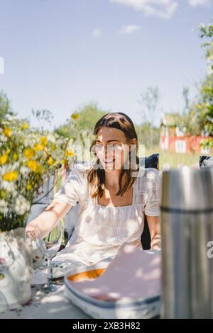Glückliche junge Frau, die an sonnigem Tag am Esstisch sitzt Stockfoto