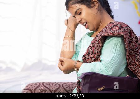 Eine Indianerin, die ihren Ellenbogen wegen Schmerzen hält und drinnen einen schmerzhaften Ausdruck zeigt Stockfoto