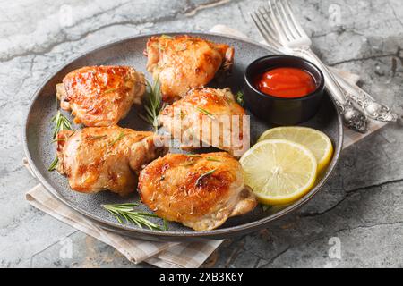 Marinierte und dann gebackene Hähnchenschenkel mit Zitrone und Rosmarin serviert mit Ketchup in Nahaufnahme auf einem Teller auf dem Tisch. Horizontal Stockfoto