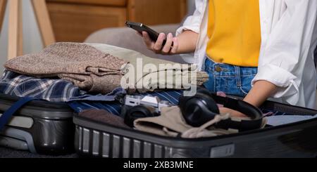 Person packt Koffer mit Kleidung und Gadgets für den Sommerurlaub, mit Smartphone für Online-Buchung von Flügen und Hotels, Konzept der Planung A Stockfoto