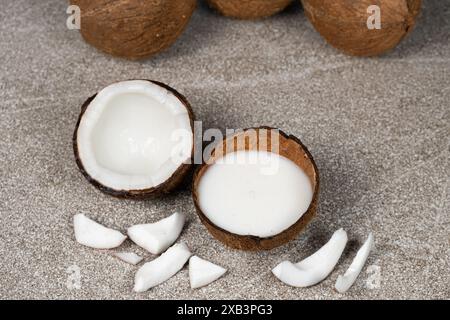 Kokosmilch in Kokosnussschale und Kokosnuss, gehacktes Fleisch auf grauem Hintergrund Stockfoto