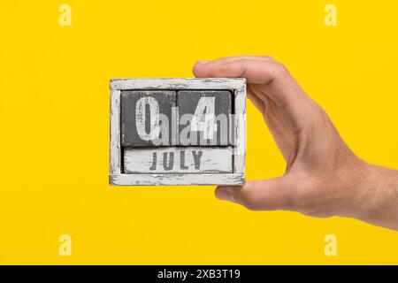 Datum ist der 04. Juli. Holzkalender in der Hand auf gelbem Hintergrund Stockfoto