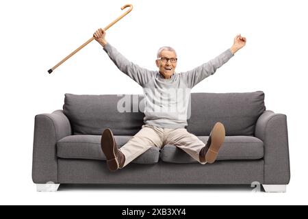 Glücklicher älterer Mann, der auf einem Sofa sitzt und einen Gehstock auf weißem Hintergrund hält Stockfoto