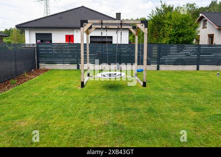 Ein moderner, quadratischer Holzspielplatz aus Metallecken, der auf dem Rasen im Hof steht. Stockfoto