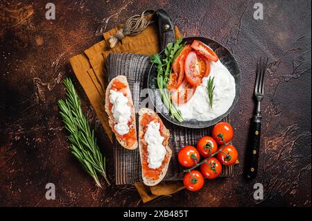 Bruschettas mit Stracciatella-Käse, gehackten Kirschtomaten und Rosmarin. Dunkler Hintergrund. Draufsicht. Stockfoto