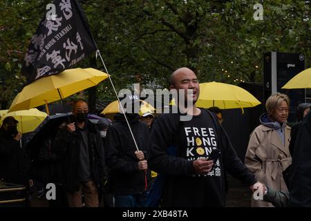 Ein Mann wurde in einem Hemd mit der Aufschrift "Freies Hongkong" gesehen, während er mit Dutzenden Demonstranten marschierte, die Flaggen trugen, auf denen stand: "Befreien Sie Hongkong, Revolution unserer Zeit", und gelben Regenschirmen, die damals von der Bewegung in Manchester wild benutzt wurden. Die Bevölkerung Hongkongs hielt vor fünf Jahren einen Protestmarsch im Stadtzentrum von Manchester ab, um der Demokratiebewegung in Hongkong zu gedenken, eine der größten Demonstrationen in der Geschichte Hongkongs. was später dazu führte, dass sich die Polizei verkrampft und viele Festnahmen verhaftet wurden, was dazu führte, dass Zehntausende von Bürgern die Stadt verließen und nach Großbritannien, Taiwan, zogen Stockfoto