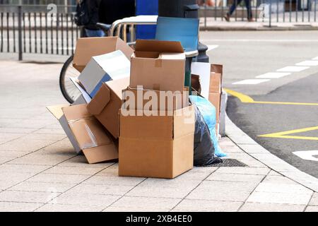 Ein Haufen Pappkartons und Plastiktüten mit Müll, der in den Müll geworfen wird, stapelt sich zufällig auf dem Bürgersteig in der Stadt neben der Straße Stockfoto