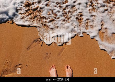 Weibliche Füße stehen auf dem Sand und Meereswellen Rollen am Strand Stockfoto