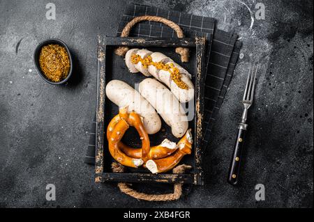 Bayerisches Gericht mit weißen Würstchen und süßem Senf in einem Holztablett mit Brezel. Schwarzer Hintergrund. Draufsicht. Stockfoto