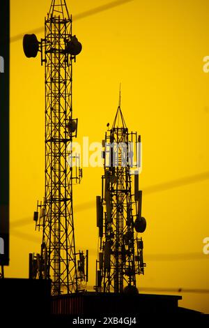 Zwei Telefontürme in Silhouette stehen hoch vor einem leuchtenden gelb-orangen Sonnenunterganghimmel. Stockfoto