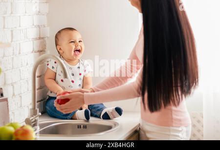 Lachendes Baby, das am Morgen mit Mutter auf der Küchenzeile sitzt Stockfoto